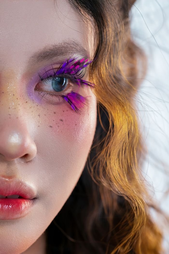 Vivid close-up of a woman with colorful eye makeup and detailed freckles.