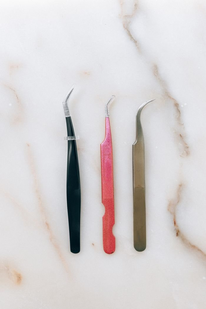 Three colorful tweezers on a marble surface, showcasing sharp stainless steel tips.