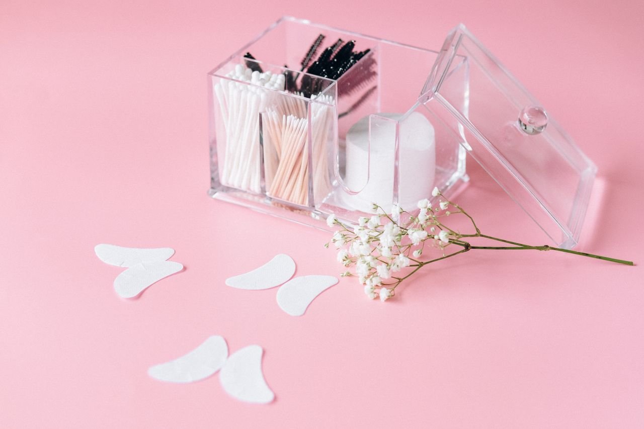 Clear makeup organizer with cotton swabs and brushes on a light pink background, with delicate baby's breath flowers.
