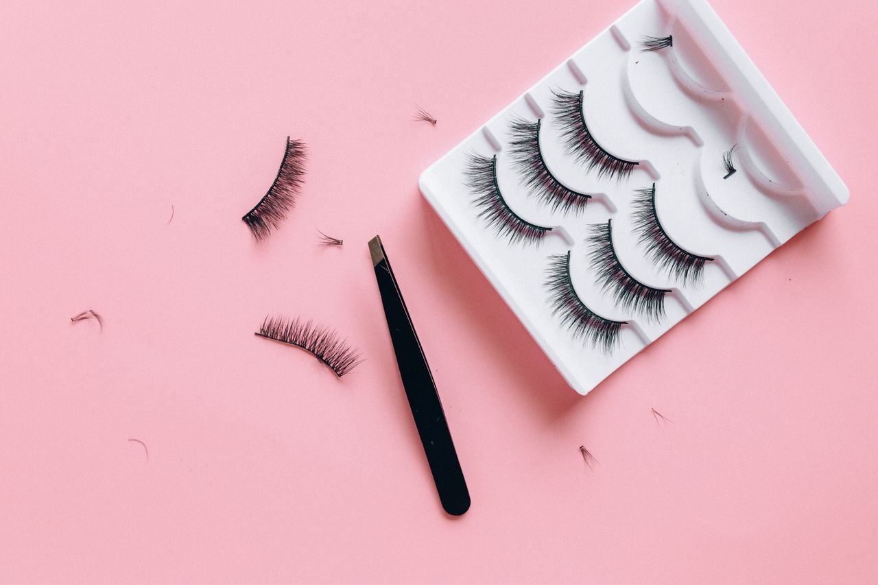 Stylish arrangement of false eyelashes and tweezers on a pink background, perfect for beauty themes.