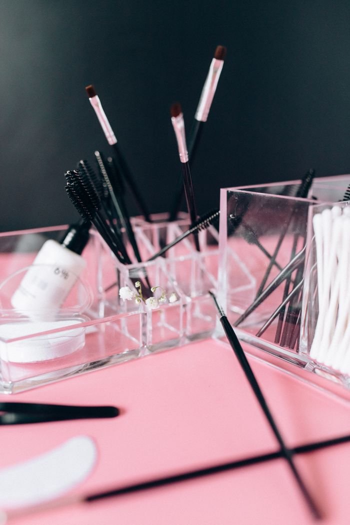 Close-up of makeup brushes, tools, and cosmetics on a pink surface.