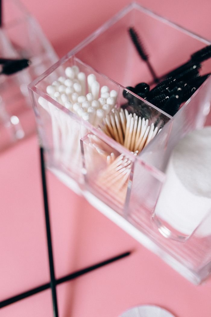 Close-up of assorted earbuds in a transparent box on a pink background.